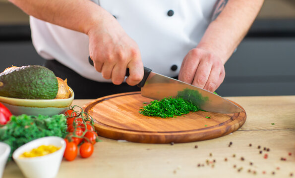 Young chef is cutting herbs and parsley in a modern kitchen. The man prepares food at home. Cooking healthy and tasty food.
