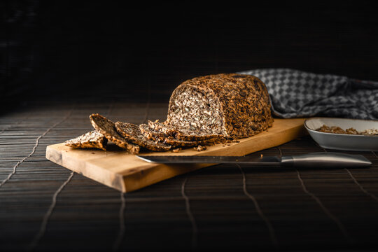 Gesundes Low Carb Brot ohne Mehl, Hefe und Sauerteig auf Holzbrett mit Messer vor dunklem Hintergrund