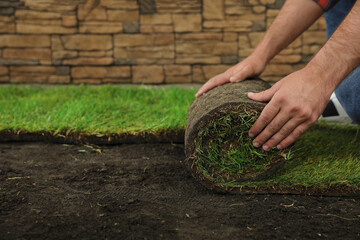 Young man laying grass sod on ground at backyard, closeup. Space for text - Powered by Adobe
