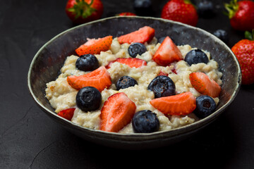 The concept of a healthy breakfast of oatmeal with strawberries and blueberries