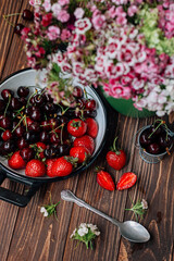 strawberries and cherries on a wooden table. flowers in a green vase.
