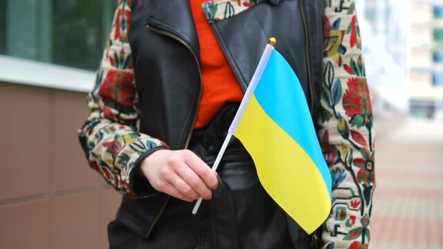 Unrecognizable woman holding Ukrainian flag. Girl walking down street with national flag of Ukraine