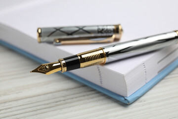 Beautiful fountain pen with ornate nib and notebook on white wooden table, closeup
