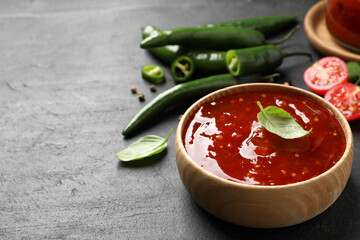 Spicy chili sauce with basil in bowl on black table, space for text