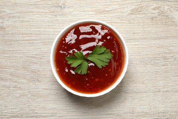 Spicy chili sauce with parsley in bowl on white wooden table, top view