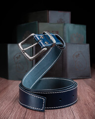 A blue leather belt with a steel buckle rests on a wooden table