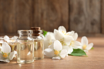 Obraz na płótnie Canvas Jasmine essential oil and fresh flowers on wooden table, space for text