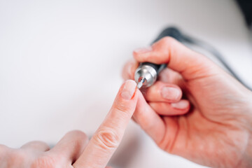 Home manicure. In the photo, a woman removes the top layer of the nail plate using a nail cutter.