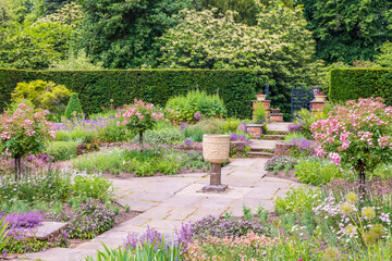 Peaceful corner of a flagged English formal garden with flower beds and a stone vase. 