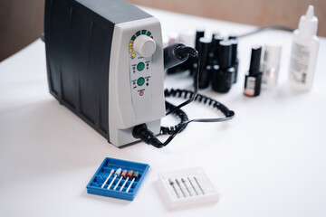 There is a manicure machine on a white table. In the foreground are boxes with attachments...