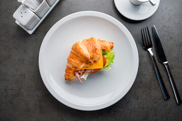 Coffee and croissant sandwich on stone table. French breakfast