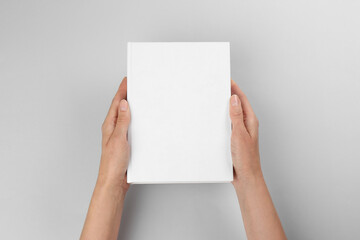 Woman holding book with blank cover on light grey background, closeup. Space for design