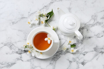 Obraz na płótnie Canvas Aromatic jasmine tea and fresh flowers on white marble table, flat lay