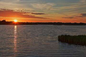 Obraz premium Beautiful orange sunrise in Russia on Volga River calm water with a Sun glow in the sky and a forest stripe on the horizon in the calm water reflection on a summer morning, Russian natural landscape