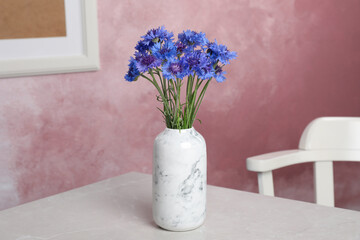 Bouquet of beautiful cornflowers in vase on light table at home.
