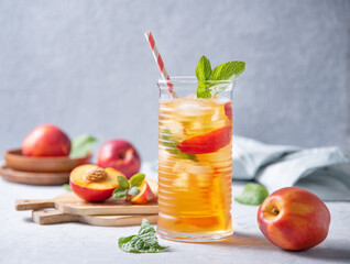 cool peach tea with mint and ice in a glass on a blue background. Front view and copy space