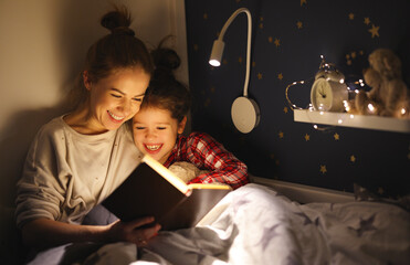 Happy mother and daughter reading book together on bed - Powered by Adobe