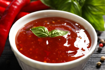 Spicy chili sauce with basil on dark table, closeup