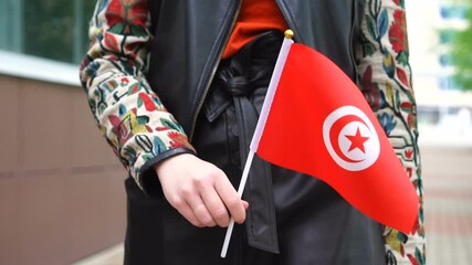 Unrecognizable woman holding Tunisian flag. Girl walking down street with national flag of Tunisia