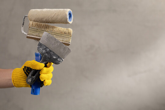 Construction worker man holding paint roller tool and concrete or plaster wall. Male hand and tools