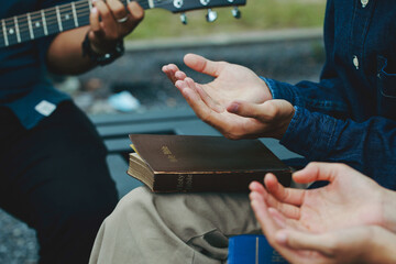 Christian families worship God in the garden by playing guitar and holding a holy bible. Group...