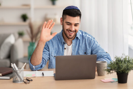 Smiling israeli man working on laptop waving hand