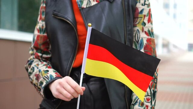 Unrecognizable woman holding German flag. Girl walking down street with national flag of Germany