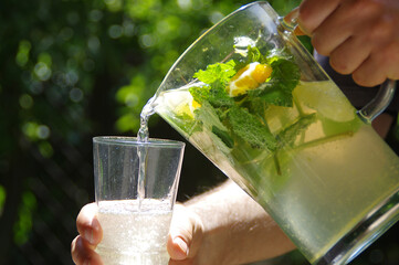 A cold lemon drink with mint leaves and fruit slices pouring into a glass - Powered by Adobe