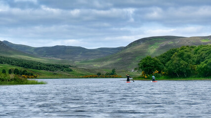Fototapeta na wymiar Man and woman paddle boarding on Loch Brora in the Highlands of Scotland
