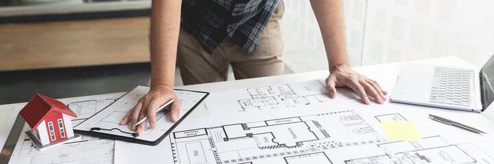 A hand holding a pencil sketching and designing a large and complex blueprint
