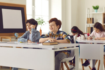 Students in class. Happy children learning new interesting stuff in a lesson. Two happy smiling elementary school boys listening to teacher sitting at desk in modern classroom. Education concept