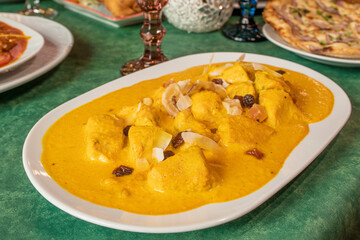 Mild yellow chicken curry, korma, cooked in a European Pakistani restaurant with dried fruit and raisins on one of the restaurant's tables.