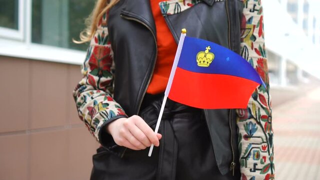 Unrecognizable woman holding Liechtensteiner flag. Girl walking down street with national flag of Liechtenstein