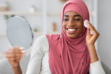 Black Woman In Hijab Holding Mirror And Cleaning Face With Cotton Pad