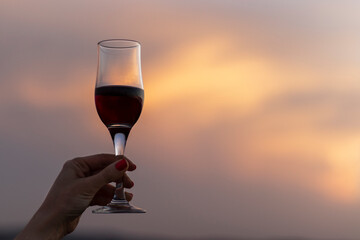 Female hand holding a glass of red wine on evening sky background. Close up.