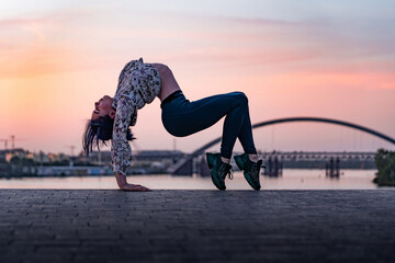 Silhouette of flexible yoga woman bending her back on dramatic sunset and cityscape. Concept of...