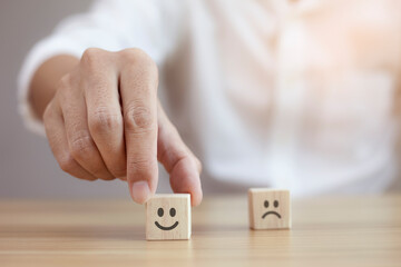Satisfaction concept, Closeup businessman choose smiley face and blurred sad face icon on wood cube.