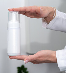 Hands hold a white bottle without labels for cosmetics. An advertising mockup. Selective focus.