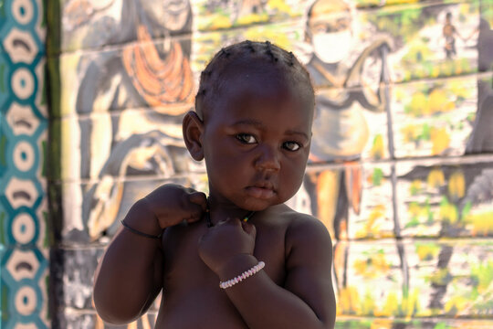 Little african black child stands near a colorful wall on a sunny day
