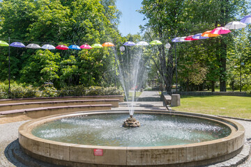 Water fountain with umbrellas in park at sunny day.