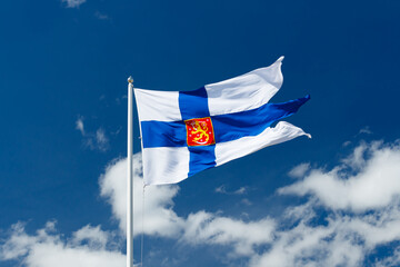 State flag of Finland with national coat of arms against blue sky on the wind