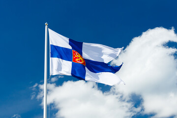 State flag of Finland with national coat of arms against blue sky on the wind