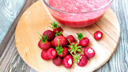 Glass cup with fruit and berry puree. Whole strawberries lie on a cutting board.