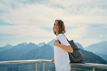 Positive female tourist smiling and enjoying fresh air at viewpoint among mountains. Adventure and...