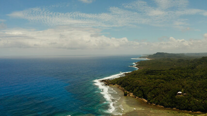Fototapeta na wymiar The coast of Siargao island with beach, green forest and ocean surf with waves against the sky and clouds, aerial view. tropical landscape.
