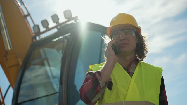 Excavator operator in hard hat talking by smartphone.
