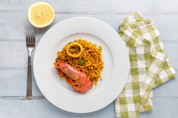 Traditional Spanish paella with seafood and vegetables served on a plate and on a blue table