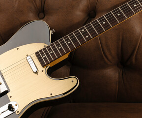 Close-up of a handmade electric guitar placed on a brown leather sofa.