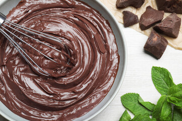 Whipping chocolate cream with balloon whisk on white wooden table, flat lay