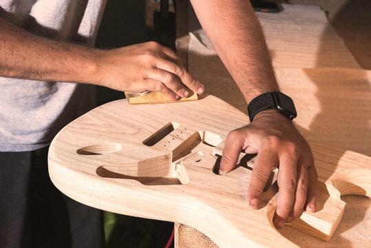Close-up of the initial hand sanding process of a guitar body.Latin man's hands holding the raw wood body while sanding it by hand. Handcrafted concept of guitar making.